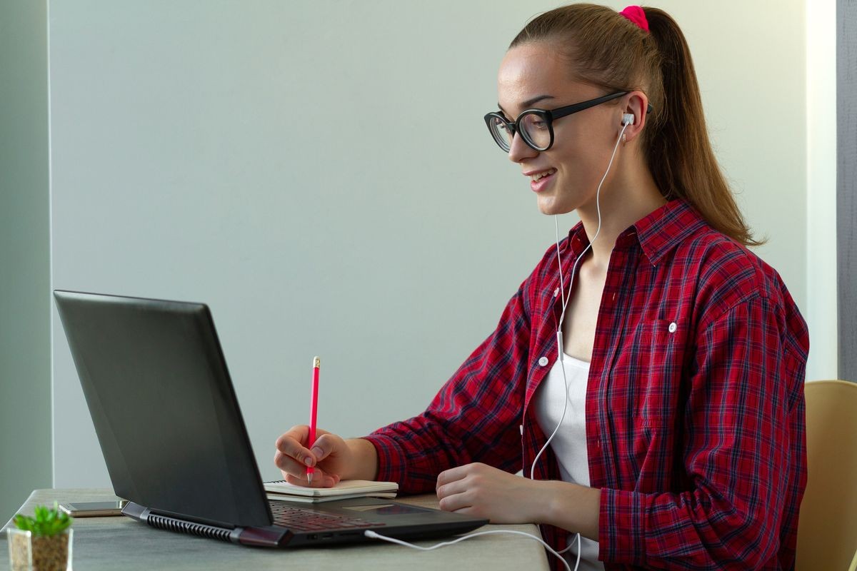 Student using online education service. Young woman looking in laptop display watching training foreign language courses and listening it with headphones. Modern study technology concept. 