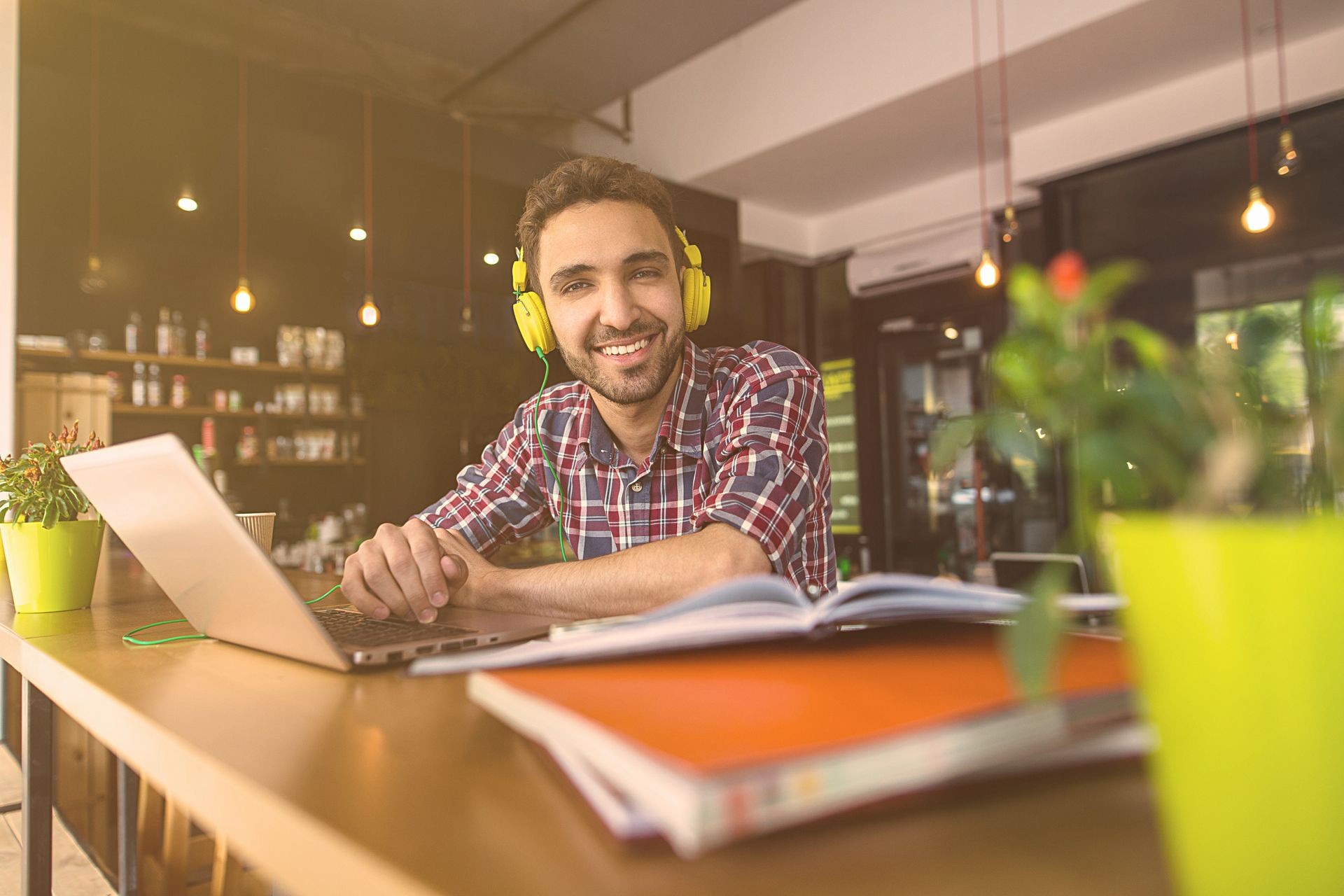 Toned image of happy smiling handsome student man studying in restaurant or cafe. Cheerful man using laptop computer for preparation for exams or classes.